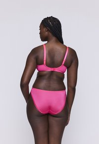 Różowa biustonosz i dopasowane majtki wykonane z gładkiego materiału. Biustonosz ma regulowane ramiączka, a majtki ozdobione są falbaną.