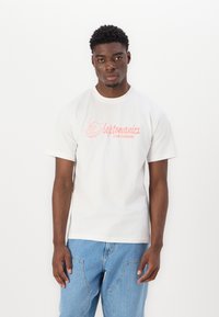 White cotton t-shirt featuring a pink illustration and text “leptomanicx CLUB CULINAIRE.” Pairing with light blue denim jeans.