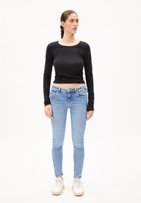 Haut à manches longues noir associé à un jean skinny bleu clair. Baskets blanches avec des semelles texturées. Design simple et ajusté avec un look décontracté.