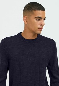 Pull en tricot bleu marine avec un col rond côtelé, présentant une texture lisse et sans motifs ni embellissements visibles.