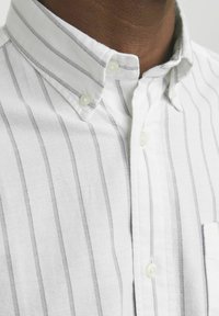 Witte overhemd met smalle grijze verticale strepen. Heeft een button-down kraag en een borstzak. De stof heeft een gestructureerde uitstraling.