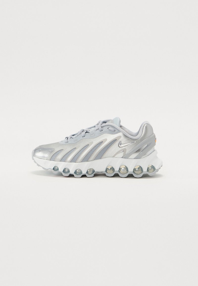 Chaussure de sport argentée et blanche avec des panneaux en mesh, une semelle à bulles unique et un petit logo swoosh sur le côté, présentée en profil sur un fond uni.