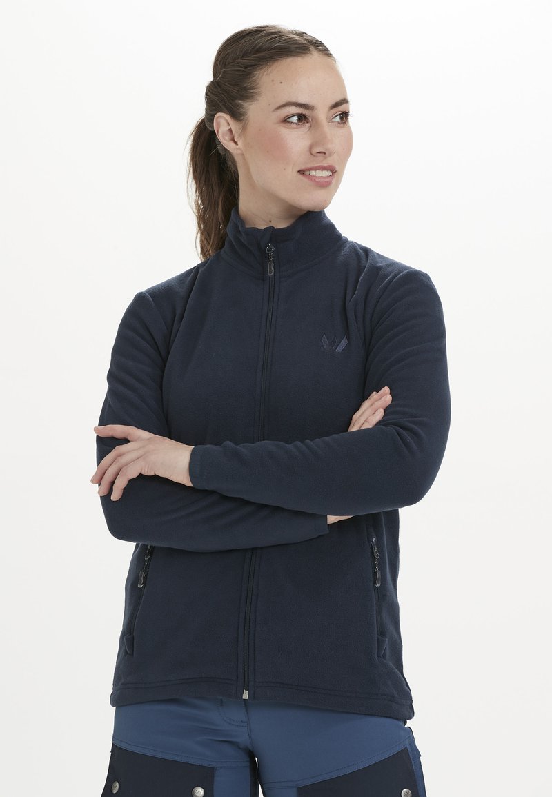 Veste en polaire marine avec col montant, zip frontal, poches latérales et détail logo subtil. Texture douce, design ajusté pour chaleur et confort.