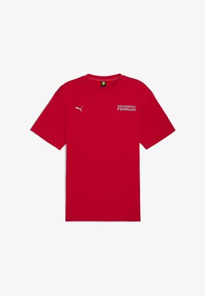 Sarkana T-kreklā ar "SCUDERIA FERRARI" logotipu un Puma logotipu baltā krāsā, klasiskā apaļā kakla un īsām piedurknēm.