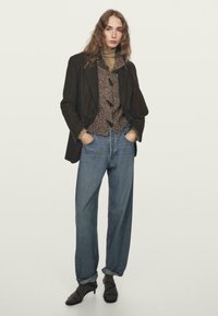 Brązowy wełniany blezer na teksturowanej, brązowej koszuli z guzikami, w połączeniu z jeansami o wysokim stanie w kolorze niebieskim i brązowymi sandałami na obcasie.