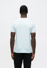 Ανοιχτό μπλε κον�τομάνικο μπλουζάκι από μαλακό ύφασμα, με λαιμόκοψη και απαλό πέφτισμα, με θέα από πίσω. Μαύρο παντελόνι δεν είναι ορατό.