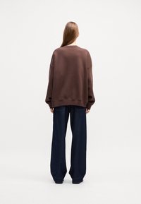 Oversized brown sweatshirt with a crew neck and drop shoulders, paired with wide-leg dark blue denim jeans without visible detailing.