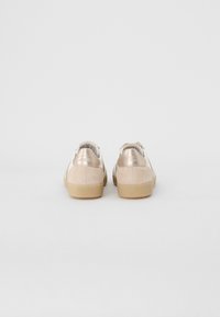 Sneakers con una combinazione di suede beige e accenti metallici. Forma arrotondata, suola in gomma e fodera in tessuto. Design minimalista.