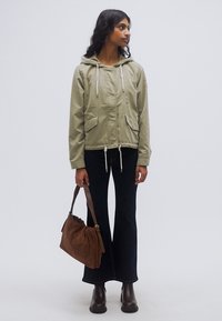 Ανοιχτό πράσινο μπουφάν με κουκούλα και κορδόνια, δύο μπροστινές τσέπες· συνδυασμένο με σκούρο καμπάνα παντελόνι και καφέ τσάντα σουέντ. Καφέ μποτάκια αστραγάλου ολοκληρώνουν την εμφάνιση.