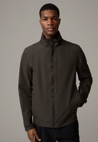 Dunkelgrüne, leichte Jacke mit hohem Kragen, Frontreißverschluss und minimalen Nähten. Sie verfügt über ein schlankes, stromlinienförmiges Design.