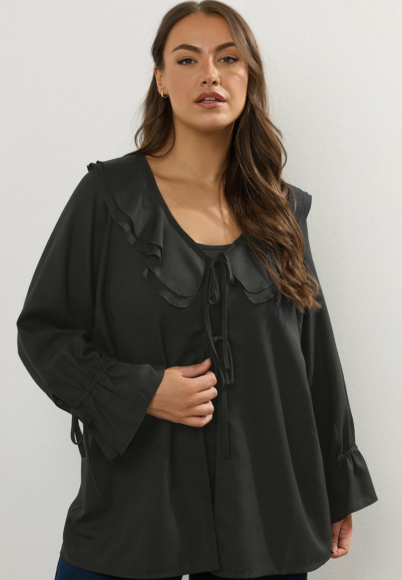 Svart långärmad blus med volangkrage, knytfram och elastiska ärmar. Mjukt tyg med en flödande silhuett.