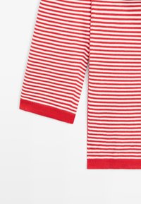 Rødt og hvidt vandret striped stof med langærmet og ensfarvet rødt ærmebånd på hvid baggrund.