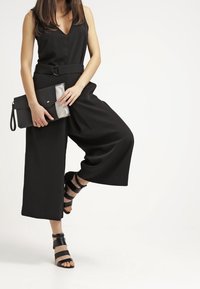 Black jumpsuit with a v-neckline, wide legs, and a belt. Paired with a black and silver clutch and black strappy heels.