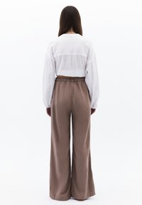 Witte blouse met lange mouwen en geplooide details op de rug, gecombineerd met luchtige, lichtbruine wijde broek. Soepele textuur.