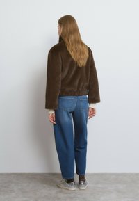 Chaqueta de piel sintética marrón con mangas extragrandes, combinada con vaqueros de corte holgado en azul. El conjunto incluye zapatillas deportivas de purpurina gris claro.