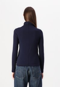 Marinblå langermet topp med høy krage, tettsittende design og myk tekstur. Kombinert med lyseblå, løstsittende denim jeans.