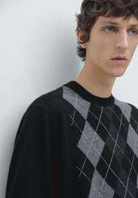 Black and grey argyle-patterned sweater made of soft fabric, featuring a ribbed neckline and unique diamond shapes, with contrasting stitching details.