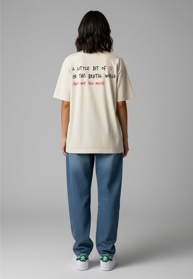 Cremfarbendes Oversized-T-Shirt mit schwarzem und rotem Textdesign auf dem Rücken. Kombiniert mit locker sitzenden blauen Jeans und weißen Sneakers.