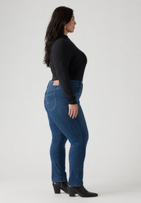 Blue denim jeans with a slight stretch fit, high waist, and five-pocket design, paired with a black long-sleeve top and black heeled boots.