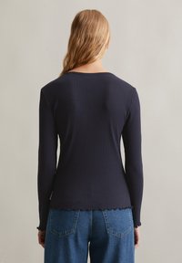 Marineblaue gerippte Langarmbluse mit gewelltem Saum und rundem Ausschnitt, die ein tailliertes Design und einen strukturierten Stoff zeigt.