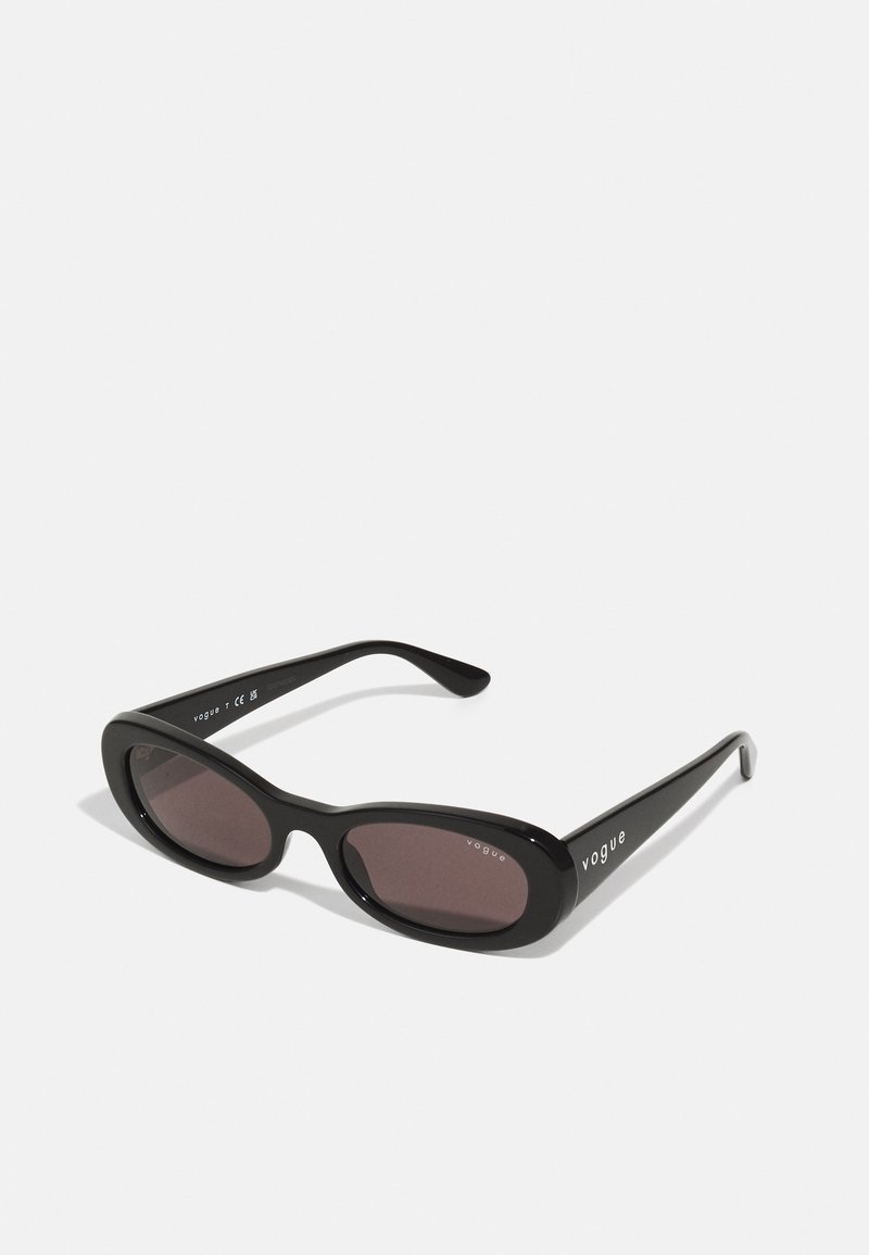 Black sunglasses with oval frames, dark tinted lenses, and "vogue" printed in white on the outer arms. Smooth plastic material.