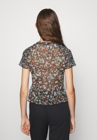 Průhledný černý květinový top s krátkými rukávy, kulatým výstřihem a nařaseným lemem. Květnový vzor obsahuje červené, bílé a zelené akcenty.