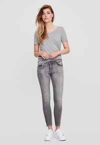 T-shirt cinza de manga curta combinado com jeans skinny cinza claro, apresentando uma textura ligeiramente esbatida e sapatilhas brancas. Design simples, estilo casual.