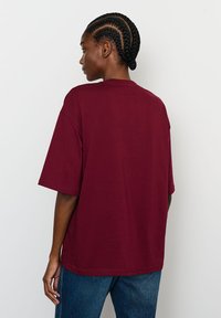 Burgundi oversized marškinėliai trumpomis rankovėmis, švelnios medvilnės tekstūra, apvalus iškirpimas ir laisvas siluetas. Puikiai tinka kasdienei aprangai.