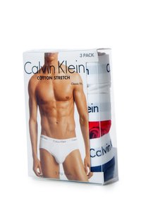 Tre confezioni di slip in cotone elasticizzato Calvin Klein in bianco, rosso e blu navy, presentate in un imballaggio trasparente con un modello maschile sull'etichetta.