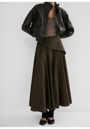 Personne portant une veste en cuir noire raccourcie, une jupe superposée marron foncé, un débardeur taupe, des ballerines noires et des leggings noirs.