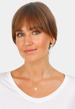 Goldener runder Anhänger mit einer zarten Kette, getragen über einem weißen Hemd. Das Modell hat kurzes braunes Haar und blaue Augen. Einfaches Design.