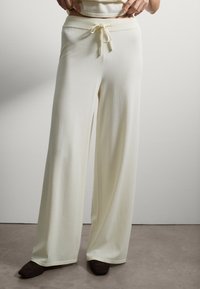 Pantalons larges de couleur crème claire en tissu doux, dotés d'une taille élastique avec cordon de serrage, texture lisse et sans motifs visibles.