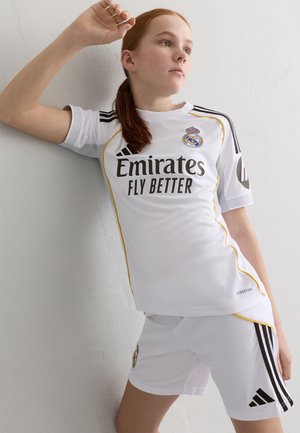 White soccer uniform with yellow accents. Features Adidas stripes, "Emirates Fly Better" logo, and Real Madrid crest. Made from breathable material.