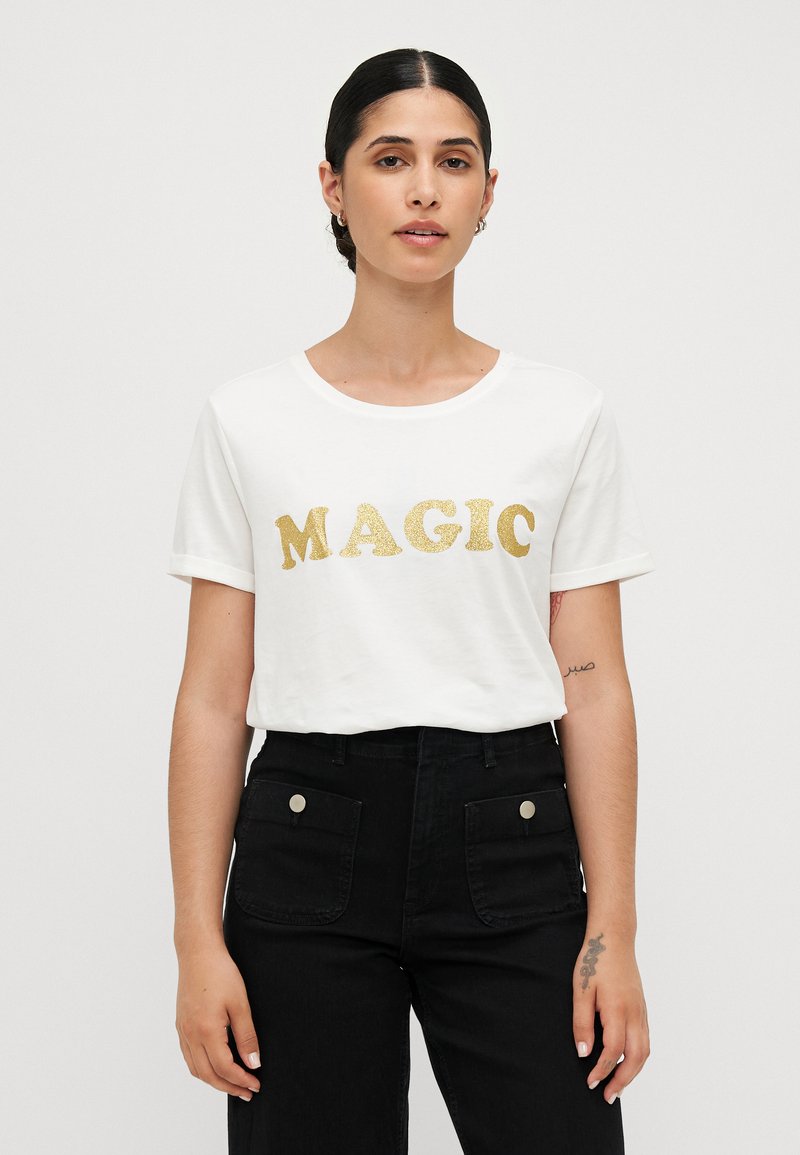 White short-sleeve t-shirt featuring the word "MAGIC" in bold, shiny gold lettering. Black high-waisted trousers with front pockets.