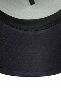 Czarna czapka z miękką podszewką i płaskim daszkiem. Zewnętrzna strona ma teksturowane wykończenie i widoczne szwy wzdłuż brzegów.