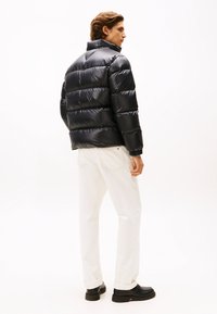 Black puffer jacket with a glossy finish, featuring a high collar and horizontal quilting. Paired with white trousers and black shoes.