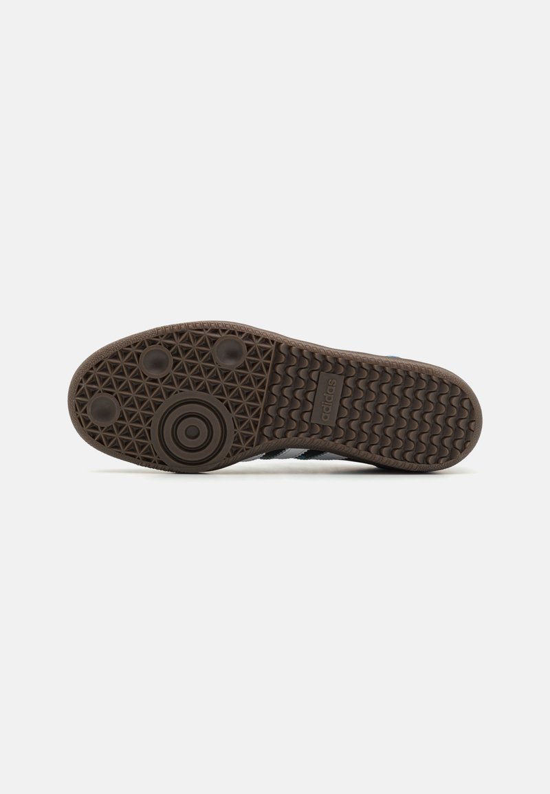 Suela de zapatilla de goma marrón con una superficie texturizada y con patrones, que presenta agarraderas circulares y triangulares para tracción y estabilidad.