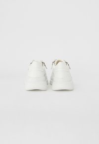 White sneakers featuring a smooth leather upper, chunky rubber sole, and metallic zipper accents at the heel. Simple and modern design.