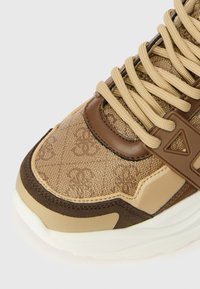 Sapatilhas em bege e castanho com um cabedal texturizado e um padrão de logotipo, biqueira reforçada e atacadores planos. A sola em borracha garante aderência.