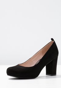 Escarpin fermé pour femme en daim noir avec talon bloc et doublure intérieure beige sur une surface blanche et un fond gris.