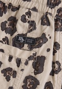 Leopardmönstrad beige tyg med mörkbruna fläckar; har en elastisk midja och en etikett med texten "Indian Blue Jeans."