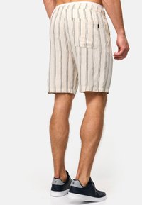Shorts rayés beiges avec taille élastique et poche arrière, associés à des baskets bleu marine avec un accent gris. Tissu texturé visible.