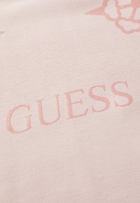 Lyserød stof med en blank tekstur, hvor ordet "GUESS" er fremhævet i en lidt mørkere pink.