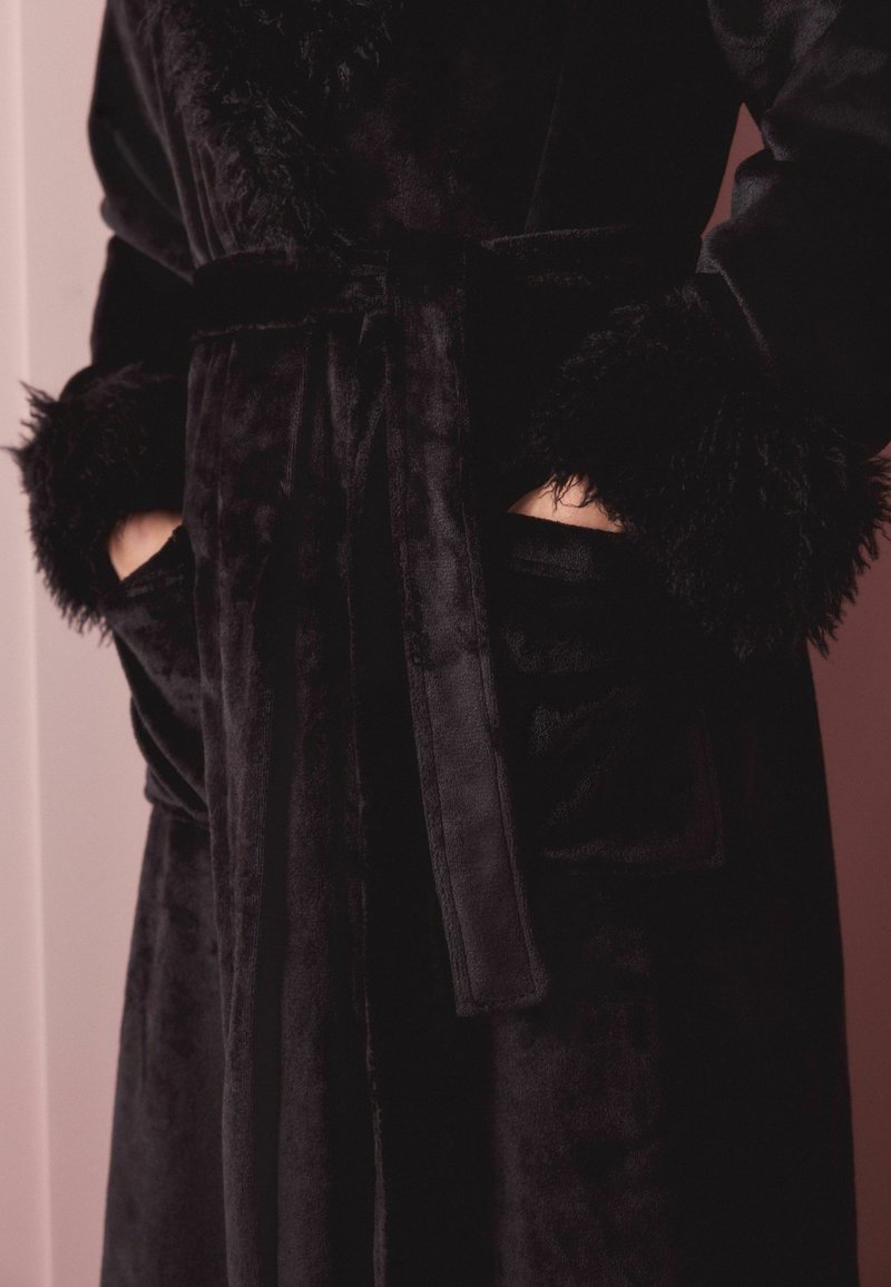 Black plush robe featuring soft faux fur cuffs, a tied waist belt, and side pockets. Smooth texture with a rich, deep color.