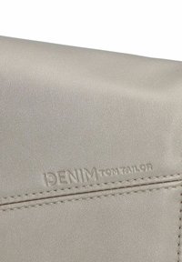 Cartera de piel sintética beige con logo en relieve "DENIM TOM TAILOR", que presenta una textura suave y detalles de costura a lo largo de los bordes.