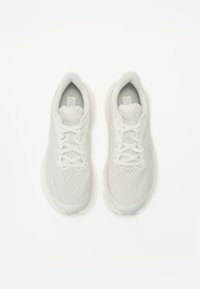 Lys grå idrettssko med en teksturert mesh-overdel og flate snørebånd, med en polstret såle og minimalistisk design.