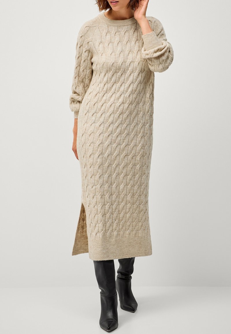 Beiges kabelgestricktes Sweatkleid mit langen Ärmeln, seitlichem Schlitz und gerippten Bündchen. Hergestellt aus weichem Stoff und mit strukturierten Mustern.