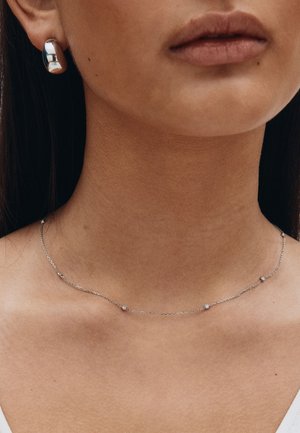 Srebrna ogrlica s sitnim okruglim perlicama i nježnim lancem, uparena s odgovarajućim sjajnim srebrnim naušnicama na pričvršćivanje. Glatka tekstura i minimalistički dizajn.