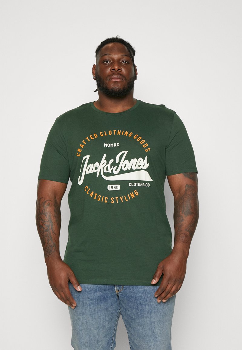 Mørk grønn bomulls T-skjorte med rund hals, med hvit og oransje grafisk tekst: "Jack & Jones" og "Klassisk stil." Korte ermer.