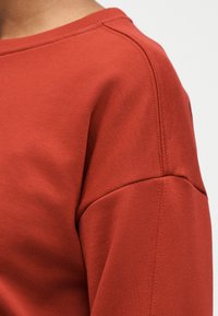 Κόκκινο φούτερ με απαλό ύφασμα, ριμπ λαιμόκοψη και ραφές σε αντίθεση. Διαθέτει άνετη ε φαρμογή και φαρδιά μανίκια.